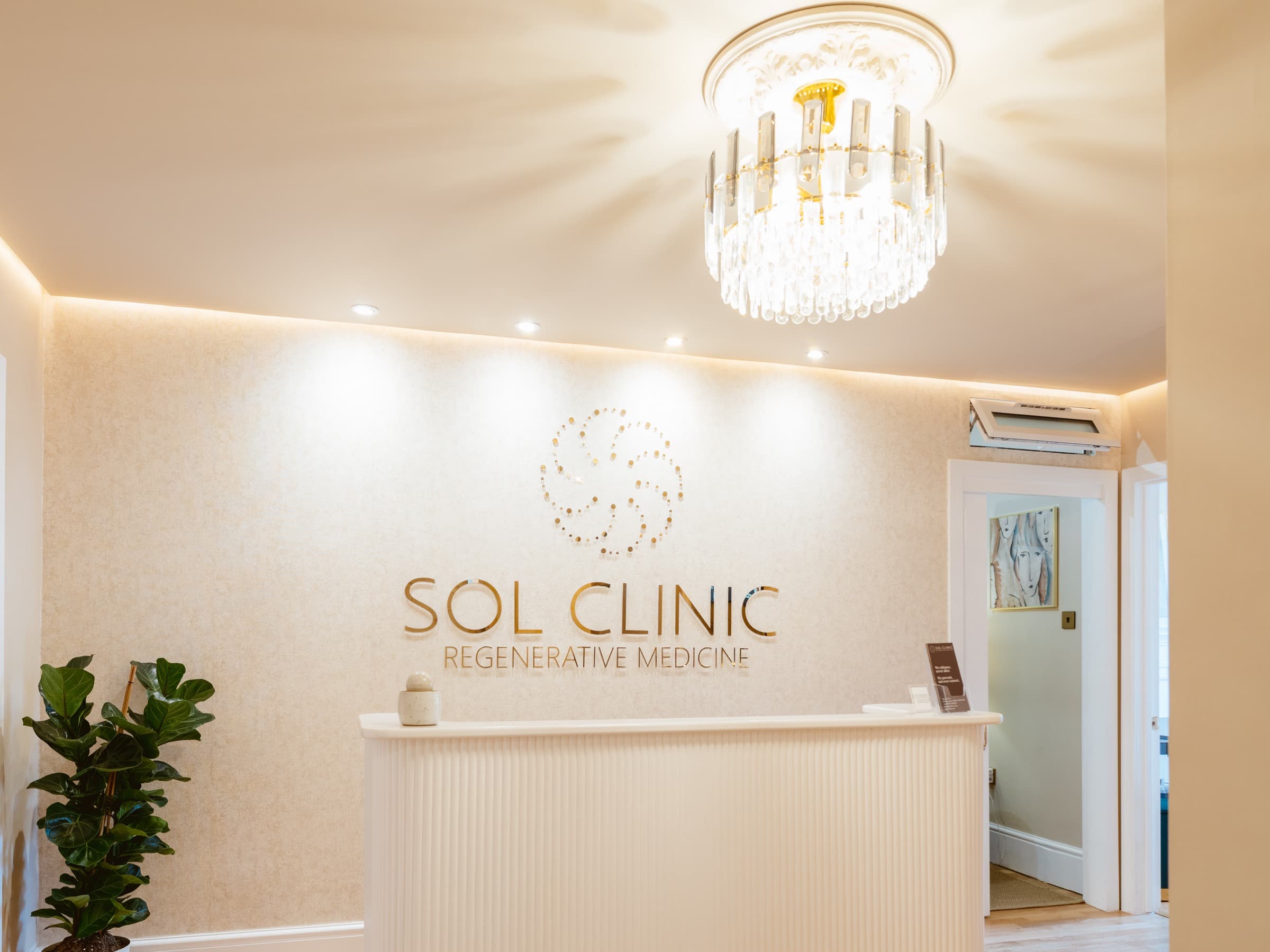 The reception at Sol Clinic London, with the illuminated Sol Clinic sign above the desk and a crystal ceiling light
